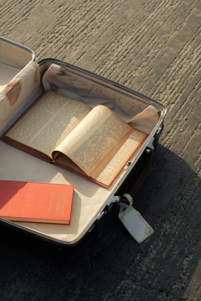 An open vintage suitcase filled with books on a textured pavement, evoking travel nostalgia.