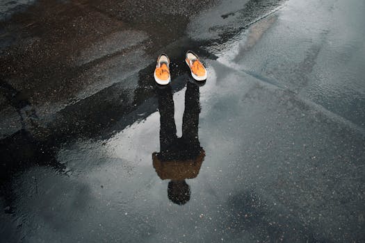 Reflection of legs and shoes in a puddle on a wet street, creating a surreal urban scene.