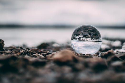 A glass sphere on a rocky beach capturing an inverted scenic reflection with a blurred background.