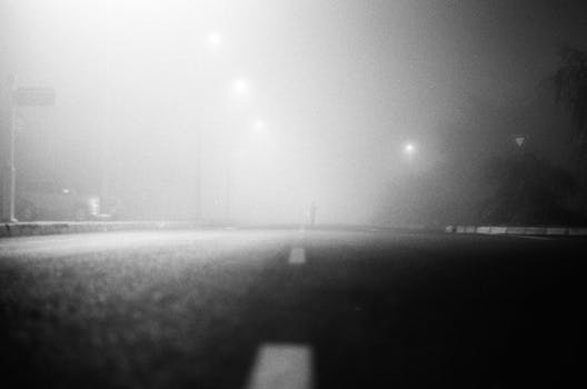 A lone figure on a foggy asphalt road at night, framed by street lamps.