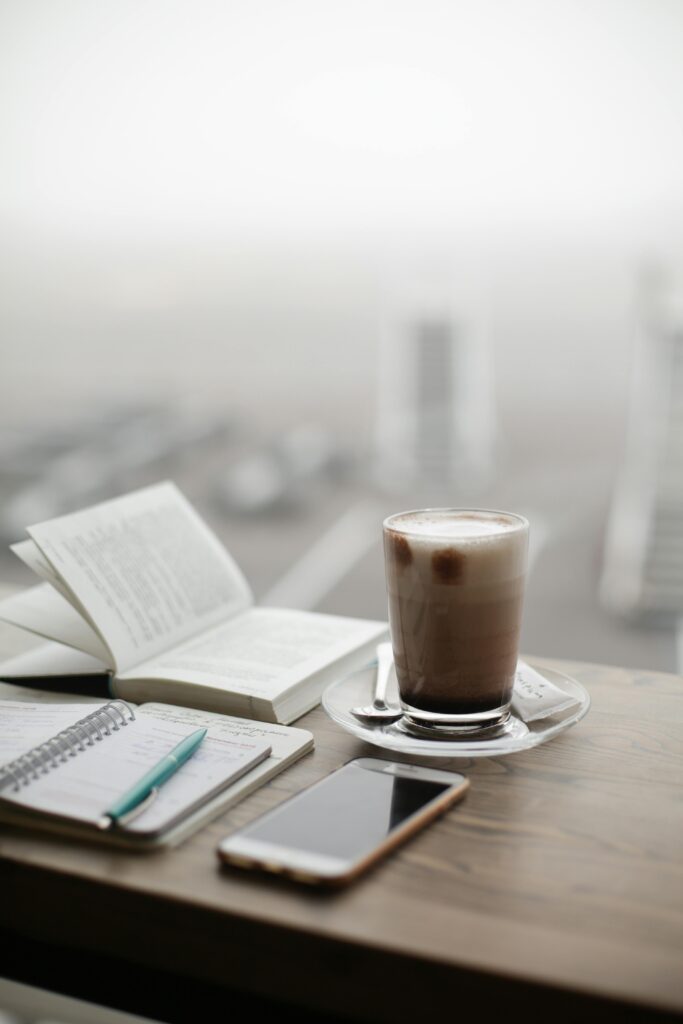 Una taza de café caliente reposa junto a un portátil y un teléfono inteligente en un día de niebla.